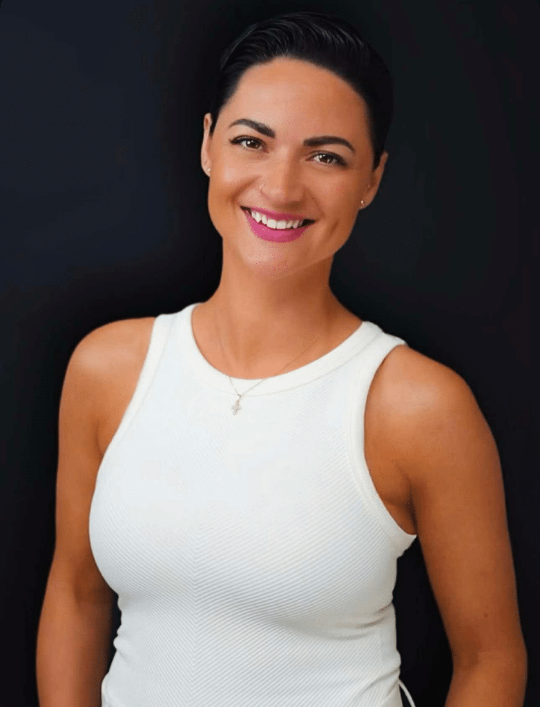 Smiling woman with short dark hair in a white sleeveless top against a dark background, portrait.